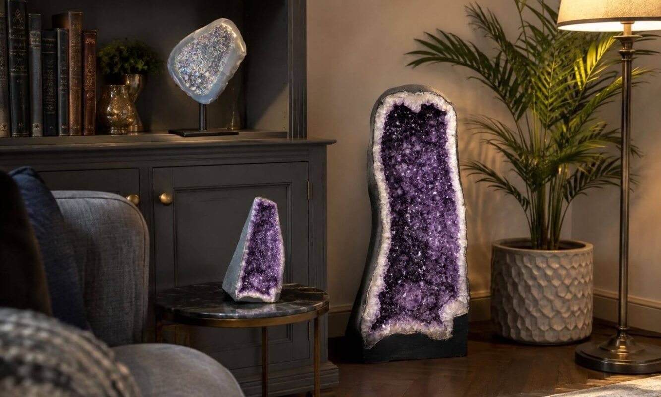 Tall amethyst cathedral, small amethyst druzy and iridescent geode on a stand displayed in a cosy living room.