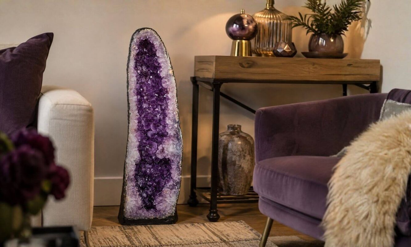 Large purple amethyst geode styled as a statement piece in a cosy living room beside a sofa, lamp and wooden console table.